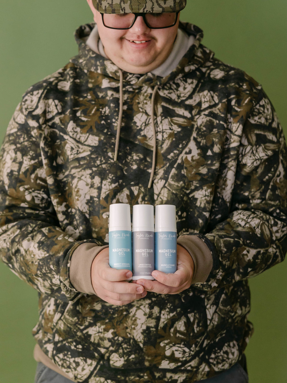 Man in camouflage holding Taylor Made Organics Sweet Dreams, Unscented, and Muscle Ease Magnesium Gels.