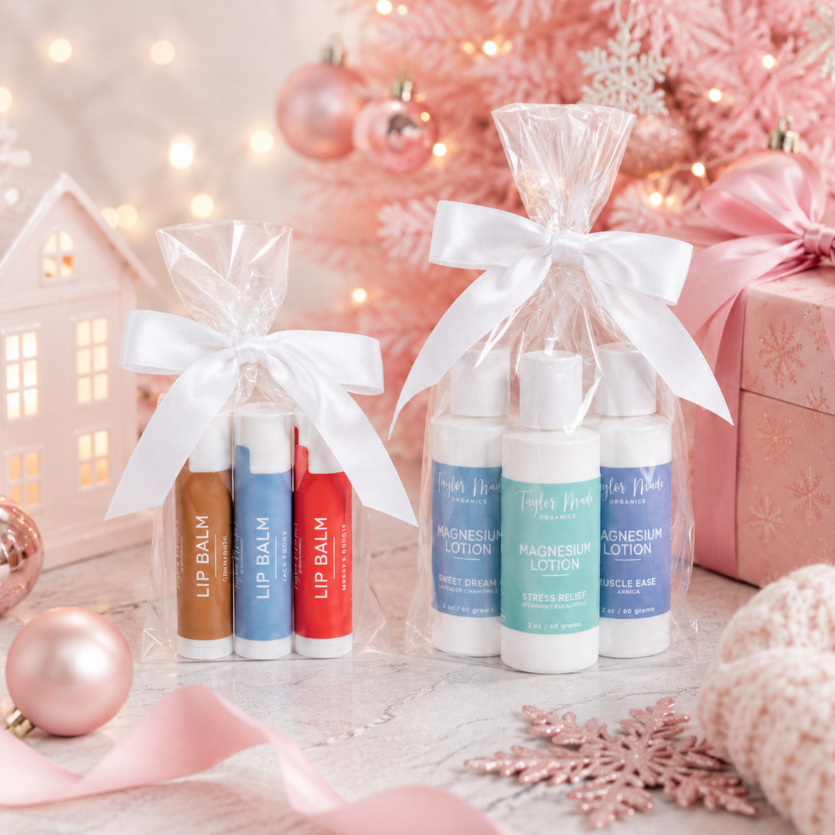 Taylor Made Organics winter lip balms and Comfort Magnesium Lotion Gift Set displayed in clear gift bags beside a pink Christmas tree.