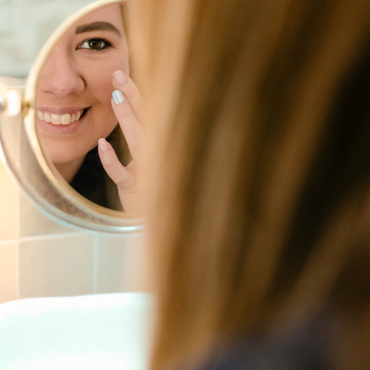 Smiling woman applying Renew face cream to her cheek while looking into a round mirror.