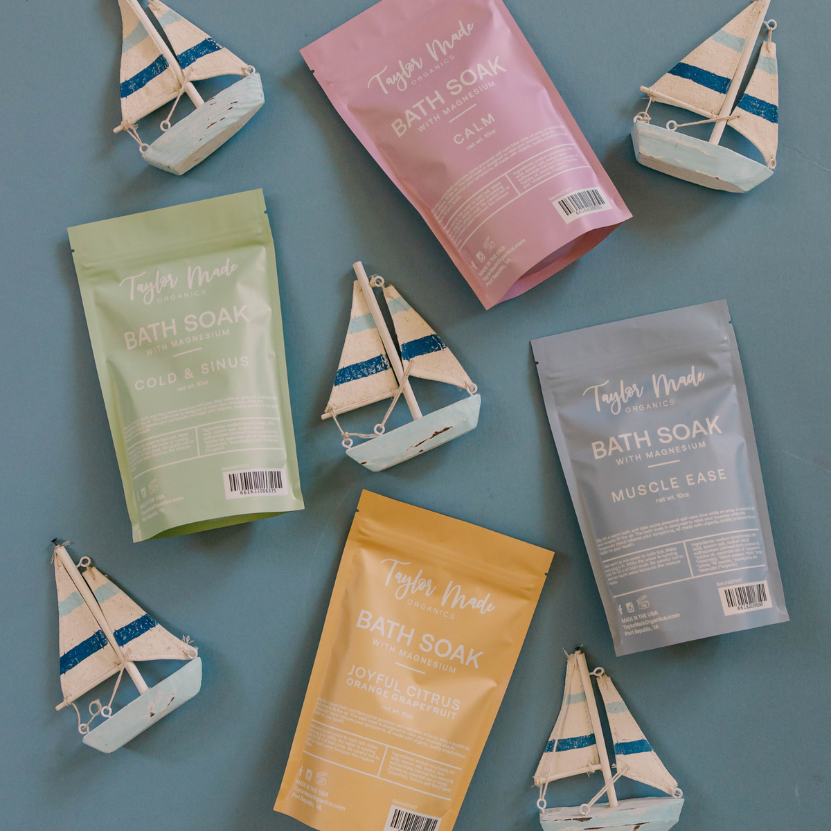 Taylor Made Organics Calm, Cold & Sinus, Muscle Ease, and Joyful Citrus Magnesium Bath Soaks with decorative sailboats.