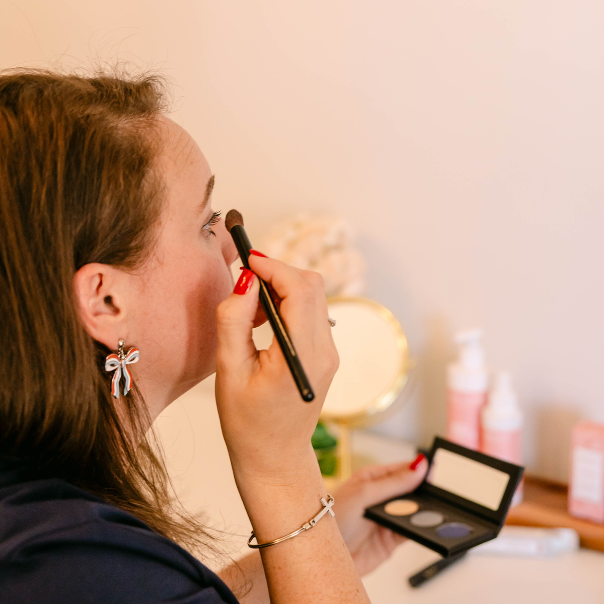Woman applying eyeshadow with a makeup brush while holding a three-shade eyeshadow palette.