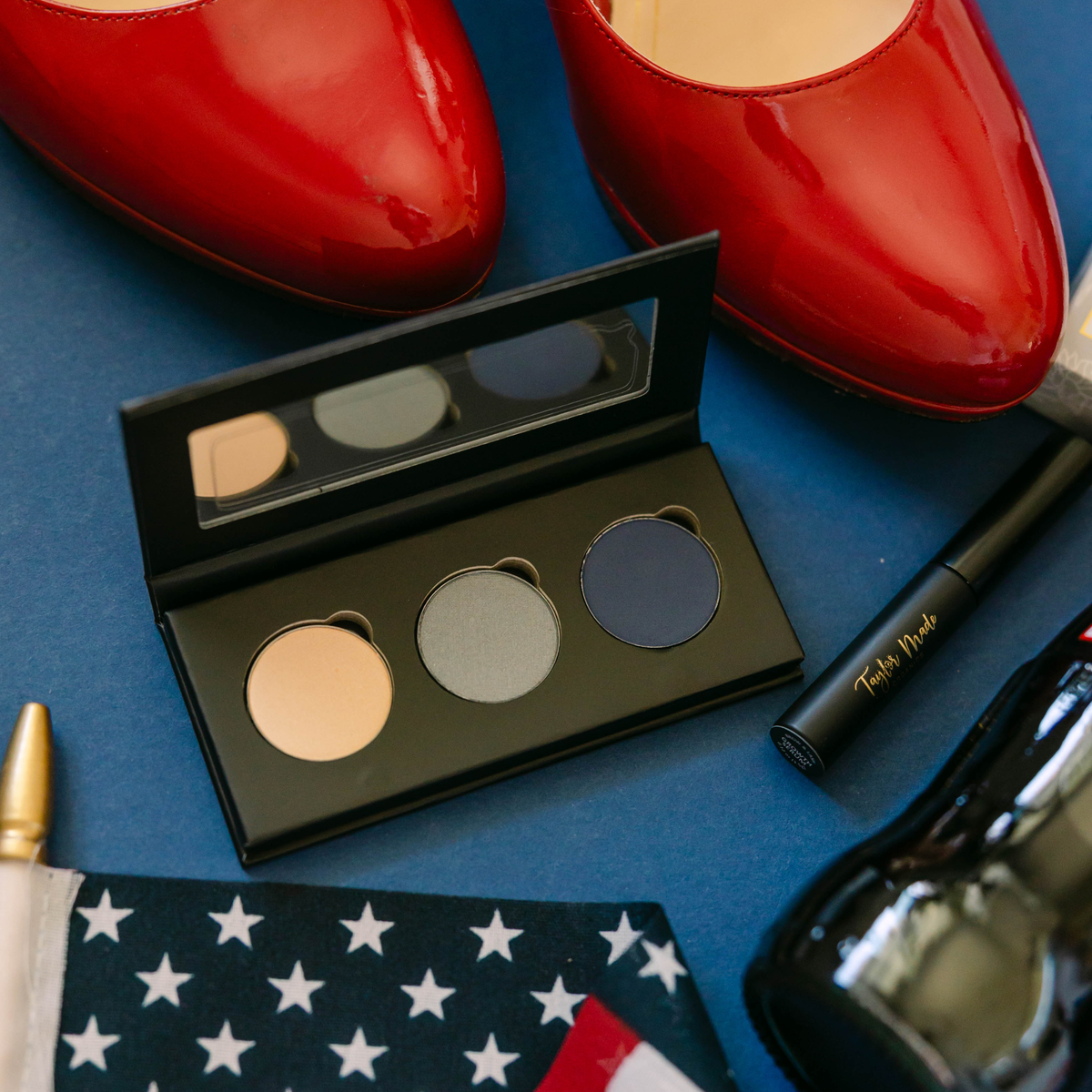 Taylor Made Organics eyeshadow palette with cashmere, silver, and sapphire shades displayed with red shoes and makeup.