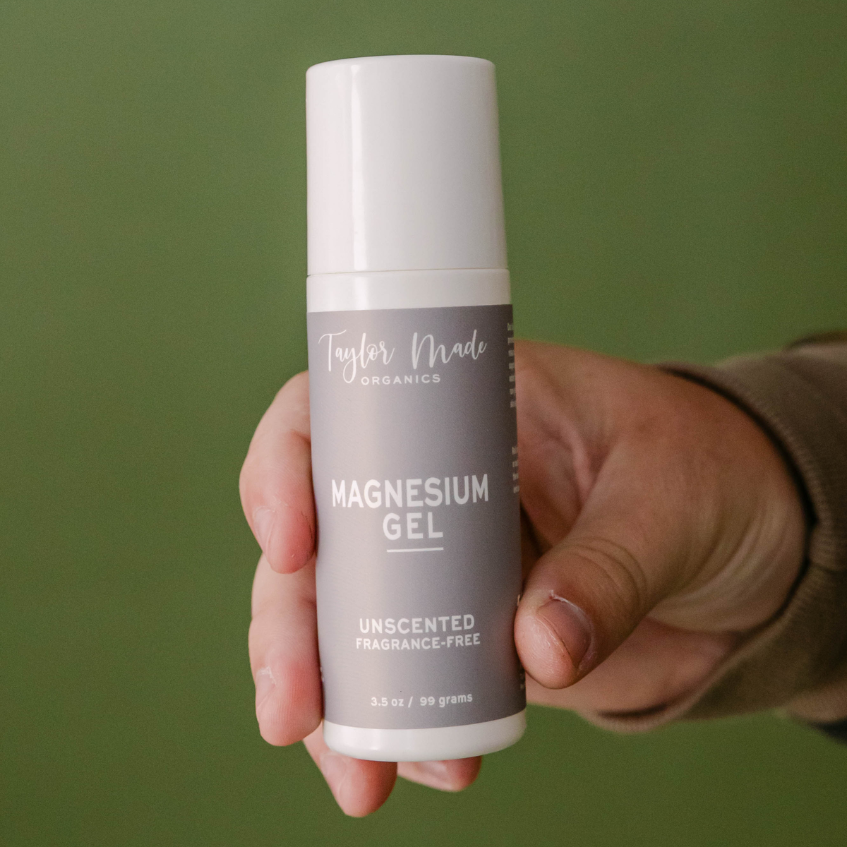 Hand holding Taylor Made Organics Unscented Magnesium Gel in a 3.5-ounce roll-on bottle.