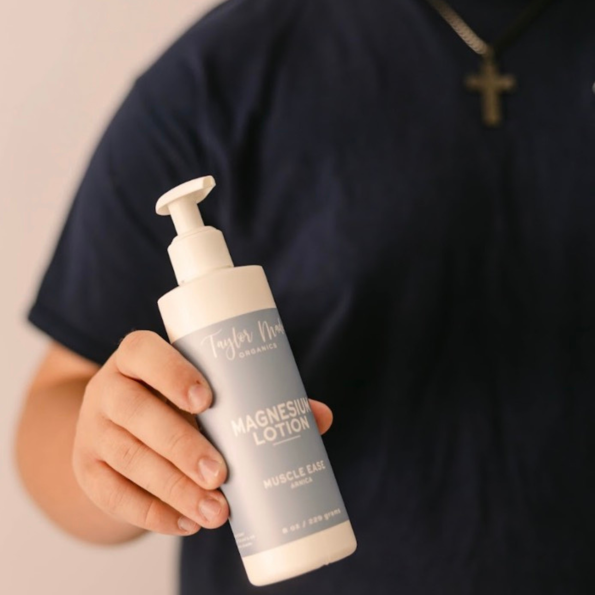 Person holding Taylor Made Organics Muscle Ease Magnesium Lotion with arnica in an 8-ounce pump bottle.