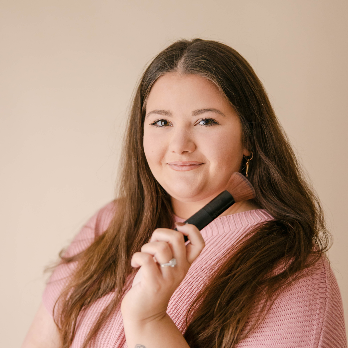 Woman applying pressed highlighter to her cheek with a jumbo flat makeup brush.