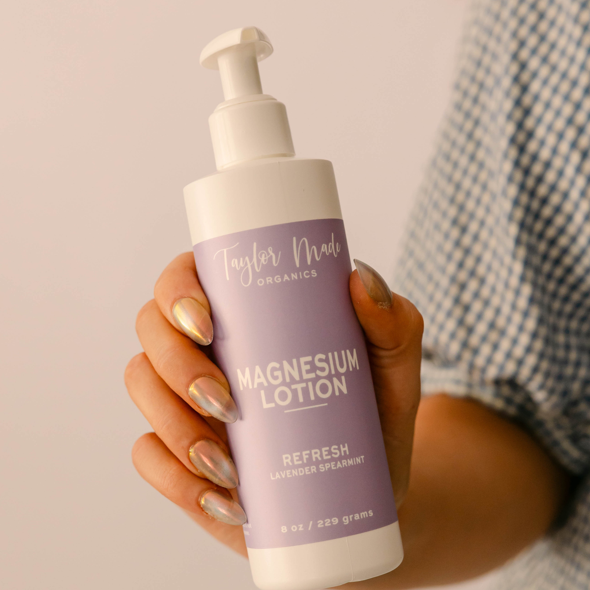 Hand holding Taylor Made Organics Refresh Magnesium Lotion with lavender and spearmint in an 8-ounce pump bottle.