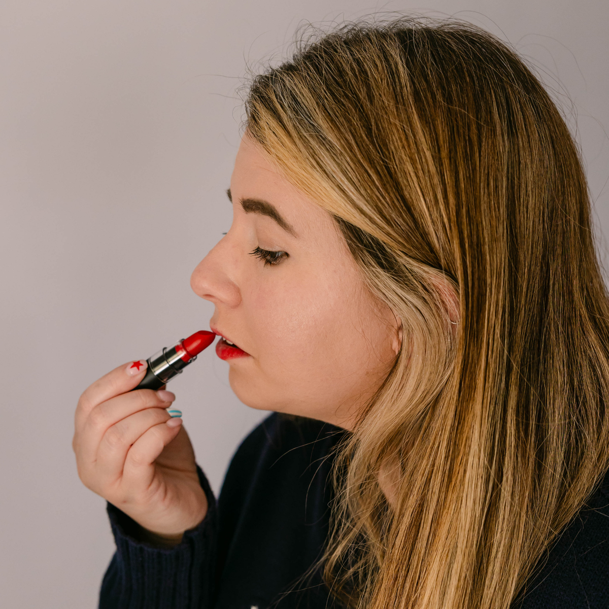 Taylor applying Taylor Made Organics Marilyn red lipstick to her lips.